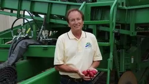 Plover River Farms Nick holding red potatoes in front of farm equipment