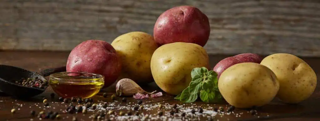 Yellow and red raw potatoes with oil, salt and pepper in rustic setting.
