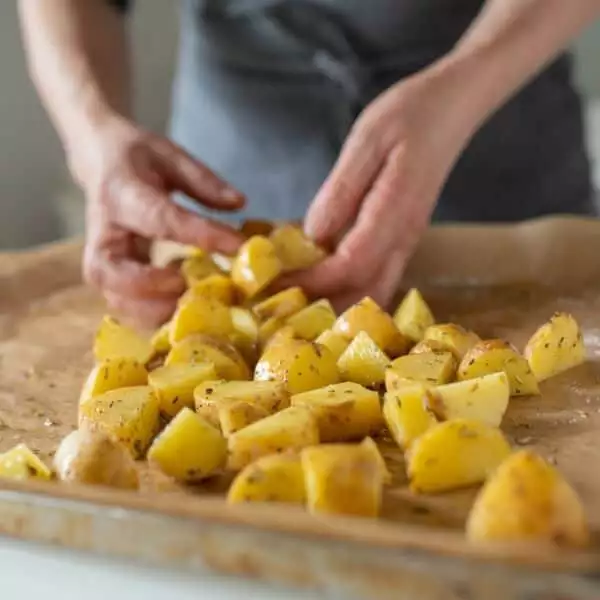 Woman preparing fresh, raw and chopped potatoes on a baking sheet for making roasted potatoes