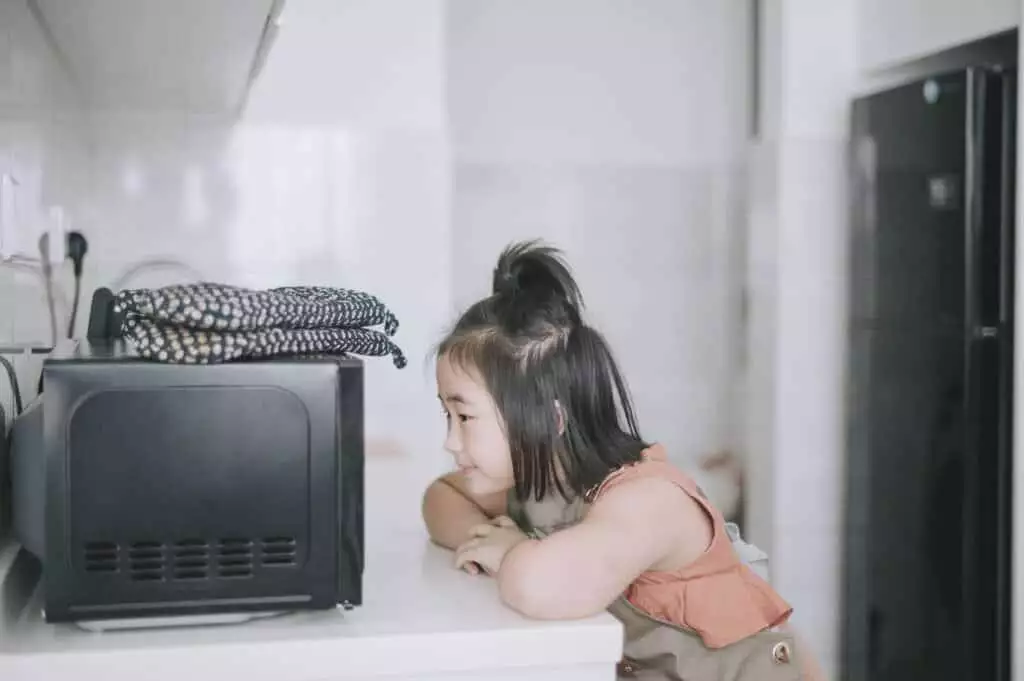 Young girl waiting for potatoes to cook in the microwave.
