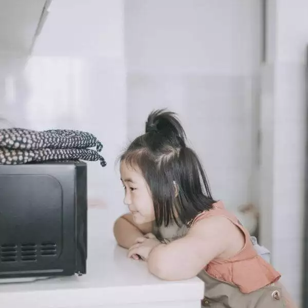 Young girl waiting for potatoes to cook in the microwave.